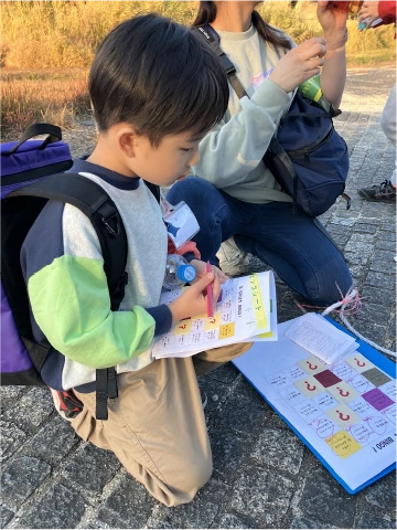 冊子を手に屋外の活動に参加する子ども